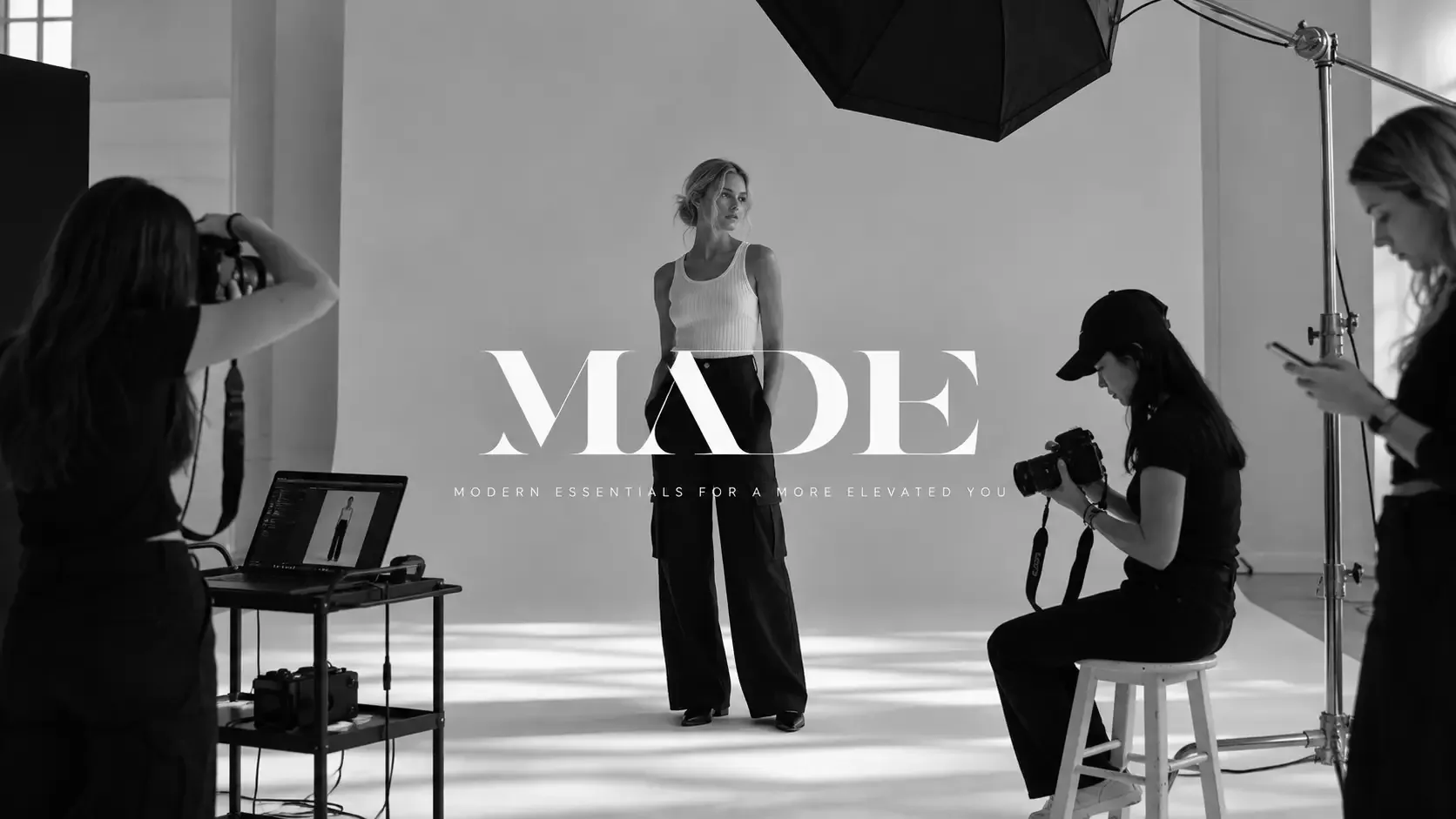 A model on a studio set with a photographer, a laptop and lights